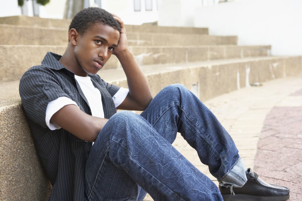 Boyhood Through Film and Pop Culture - Providence Holistic Counseling Services - Unhappy Male Teenage Student Sitting Outside On College Steps
